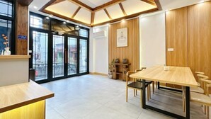 A spacious room with a wooden ceiling, a large table with chairs, a reception desk, and a view through a glass door. - Phoenix Haven (Xiangxi)