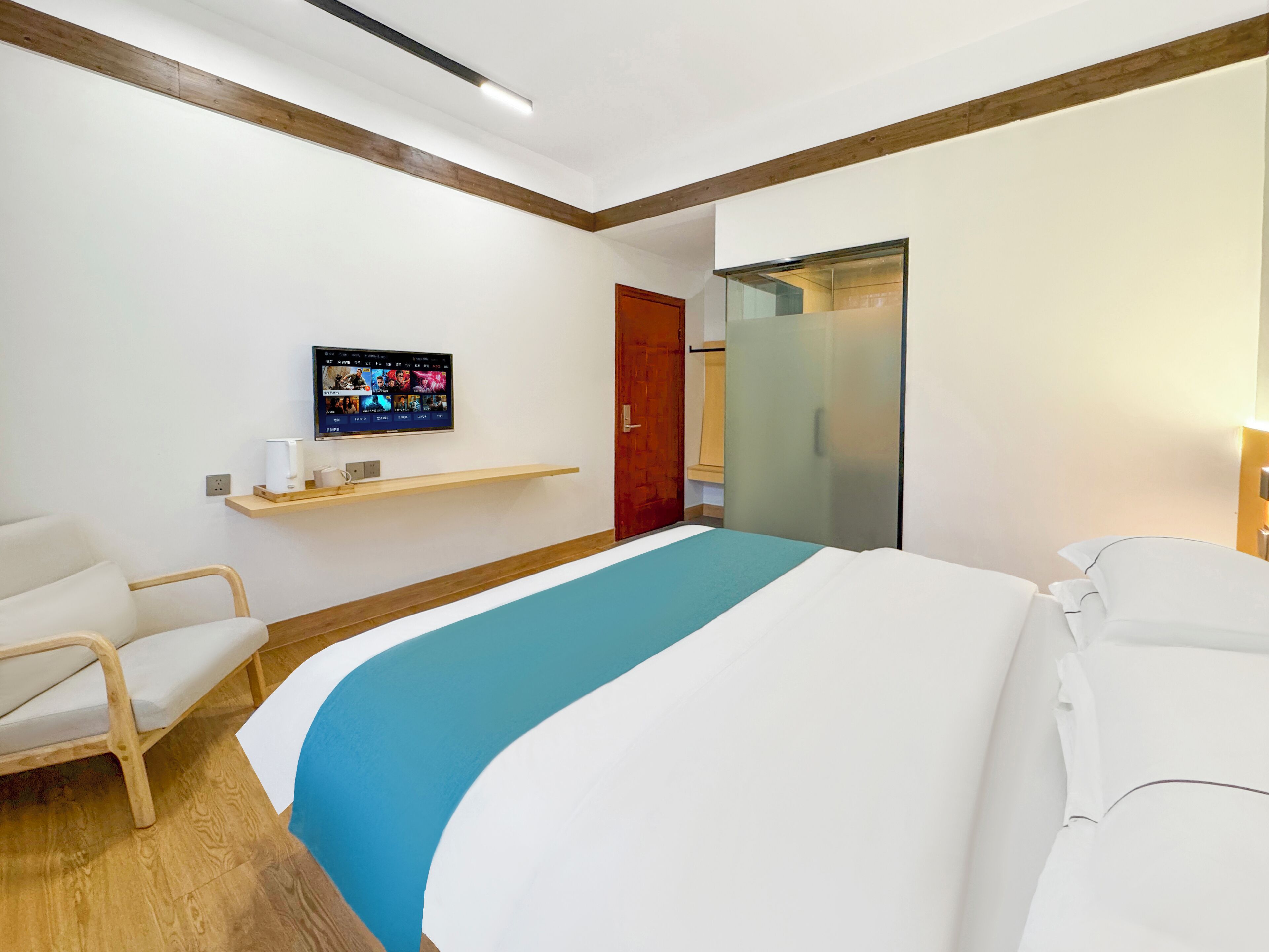 A hotel room with a bed, a TV mounted on the wall, a wooden chair, and a wooden shelf.