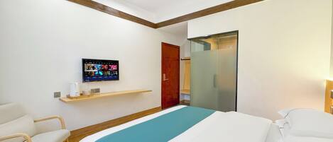 A hotel room with a bed, a TV mounted on the wall, a wooden chair, and a wooden shelf.