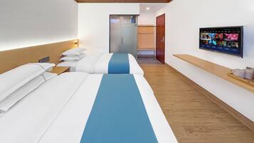 Habitación de hotel con dos camas, un televisor en la pared y suelo de madera.