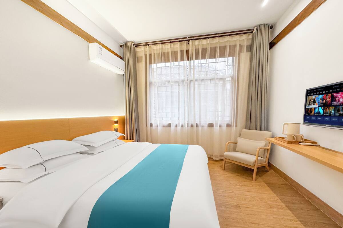 A hotel room with a bed, a chair, a TV, and a window with curtains.