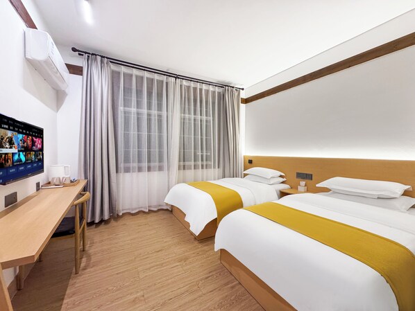 Habitación de hotel con dos camas, un escritorio, un televisor montado en la pared y una ventana con cortinas translúcidas.