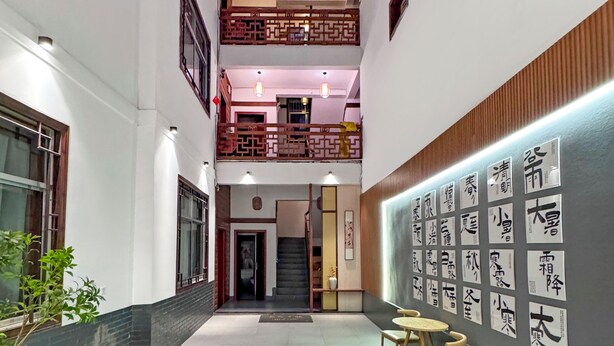 A spacious interior with a central courtyard, a staircase leading to an upper level, and a wall adorned with calligraphy. - Phoenix Haven (Xiangxi)
