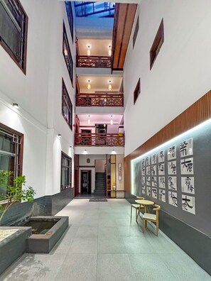 A spacious interior with a central courtyard, a staircase leading to an upper level, and a wall adorned with calligraphy. - Phoenix Haven (Xiangxi)