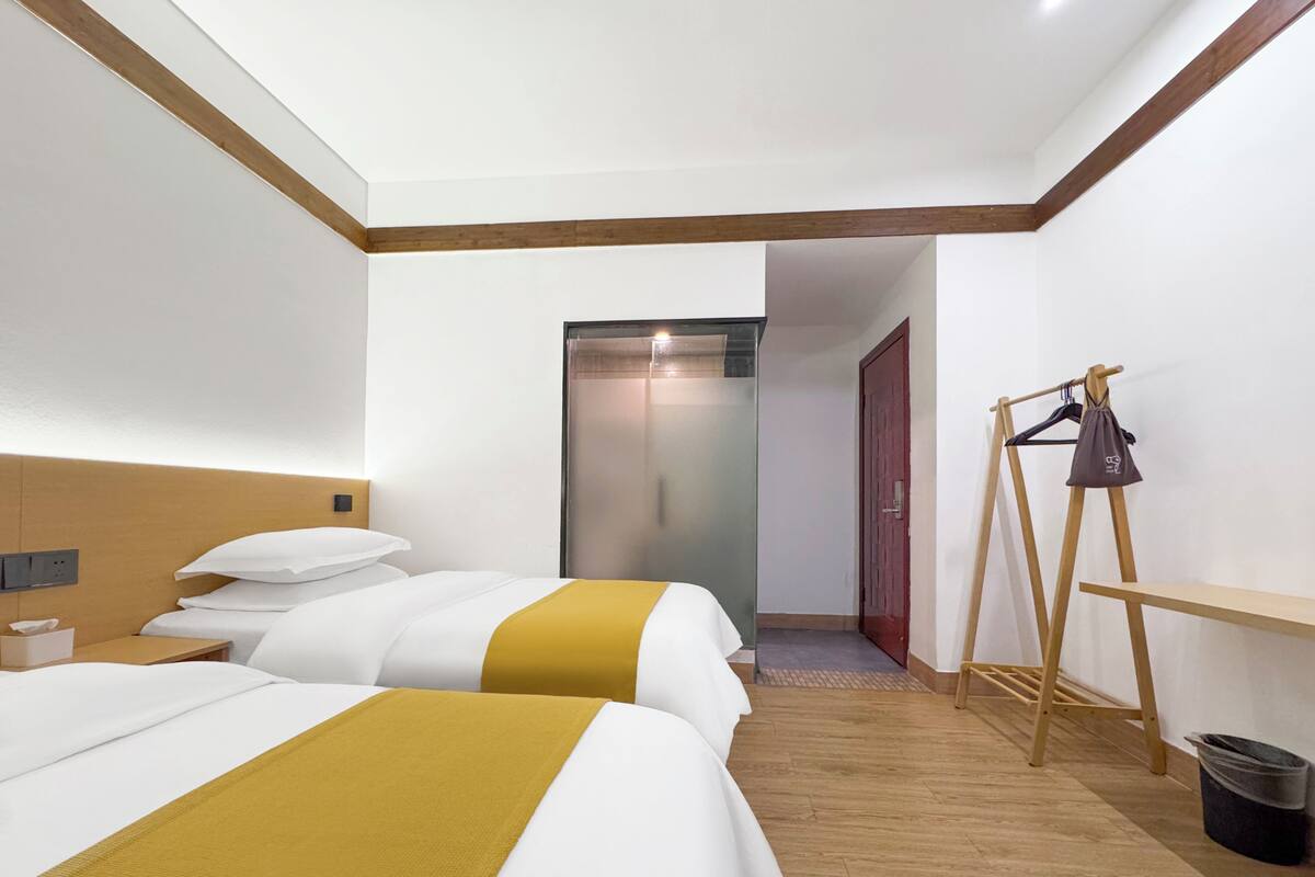 A hotel room with two beds, a wooden headboard, a wardrobe, and a small table.