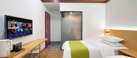 Habitación de hotel con televisión en la pared, escritorio con cafetera, dos camas con ropa de cama verde y blanca, y cabeceros de madera.