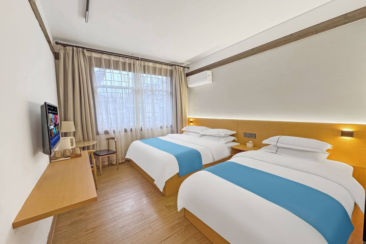 A hotel room with two beds, a desk, a chair, a TV, and a window with curtains.