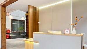 A reception desk with a wooden panel design, a white counter, and a vase with orange flowers. - Phoenix Haven (Xiangxi)