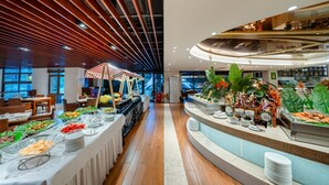 Een buffetgedeelte met diverse thematafels, een zithoek met tafels en stoelen, en een toonbank met diverse gerechten.