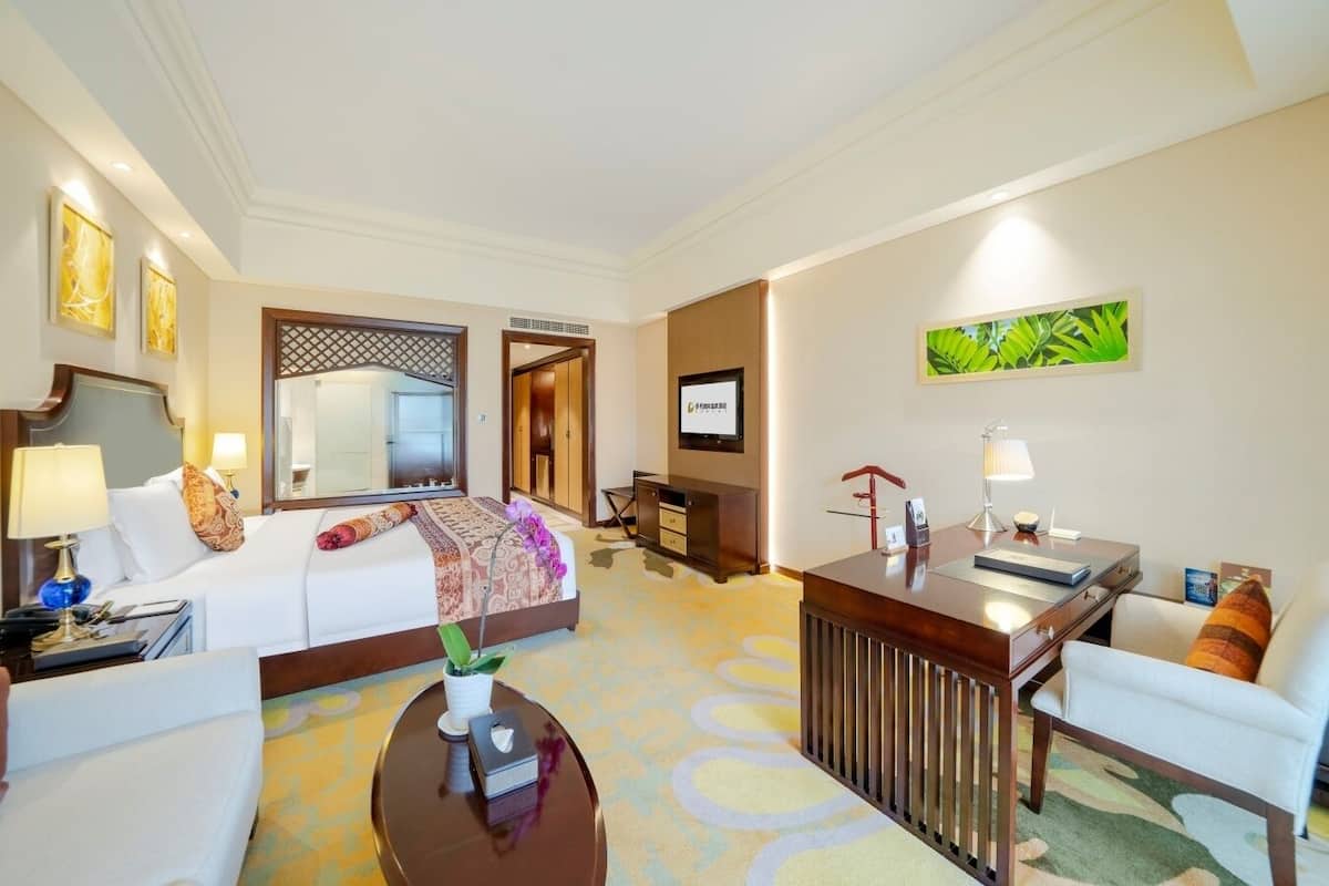 A hotel room with a bed, a desk, a chair, a coffee table, and a TV.