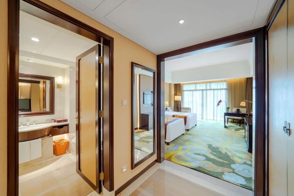 A hotel room with a large mirror, a bed, a desk, and a view of the hotel lobby.