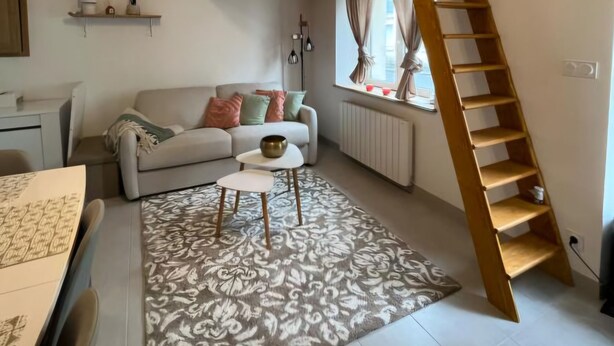 Un soggiorno moderno con un letto a soppalco, una scala in legno, un divano, un tavolino da caffè e illuminazione a sospensione.