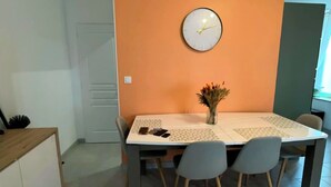 Zona pranzo con tavolo, sedie, orologio e vaso con fiori secchi.