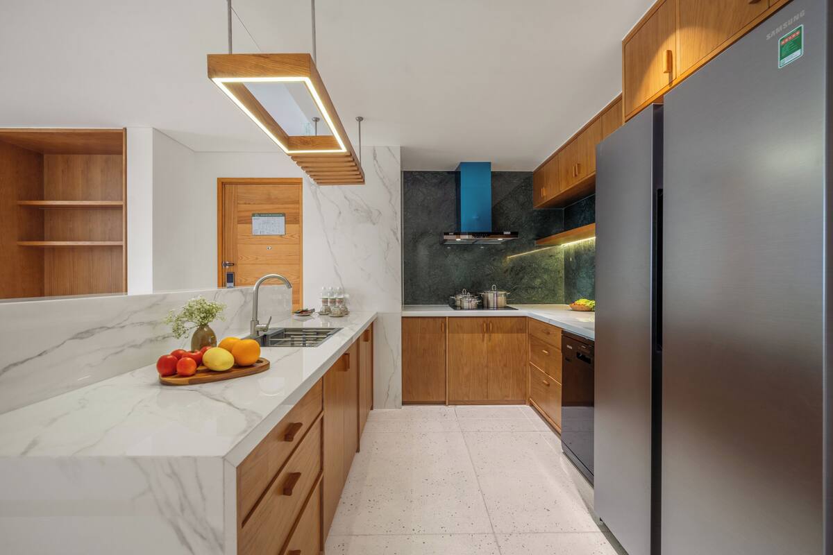 Une cuisine moderne dotée de plans de travail en marbre, d’armoires en bois, d’un réfrigérateur en acier inoxydable et d’une cuisinière encastrée.