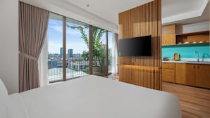 A modern hotel room with a large bed, a TV, a kitchen area, and a view of the city through large windows. - Vernal hotel & Apartment office  (Da Nang)