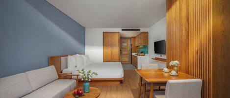 A modern hotel room with a sofa, a bed, a dining table, and a TV.