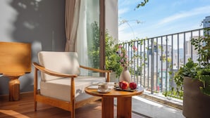 A balcony with a wooden chair, a small round table with fruits, and a vase of flowers. - Vernal hotel & Apartment office  (Da Nang)