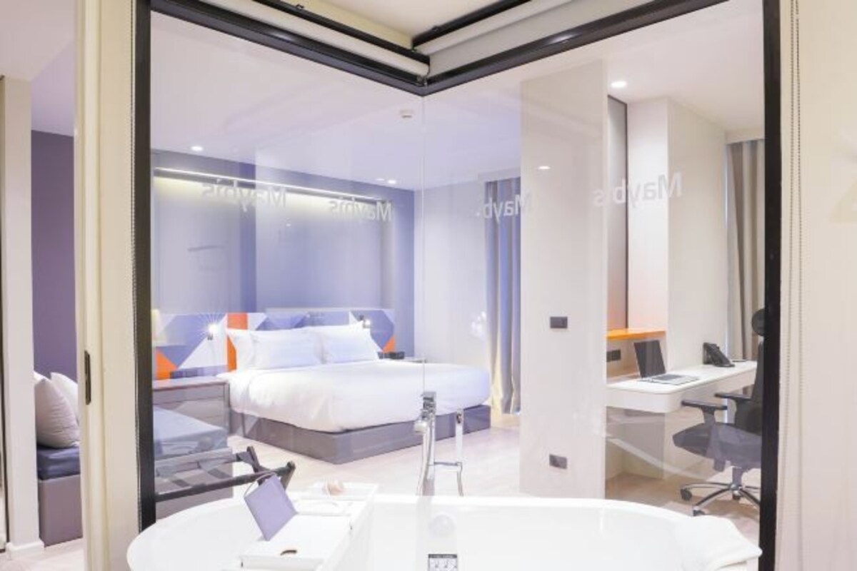 A modern hotel room with a bed, a desk, and a bathroom.
