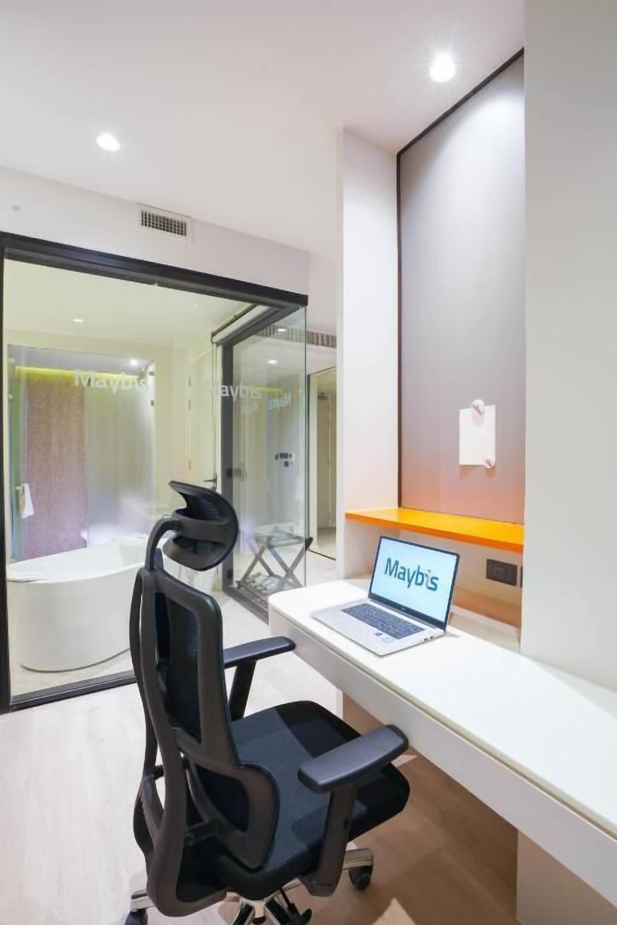 Een moderne kantoorruimte met een wit bureau, een zwarte bureaustoel en een laptop waarop "Mayb's" staat.