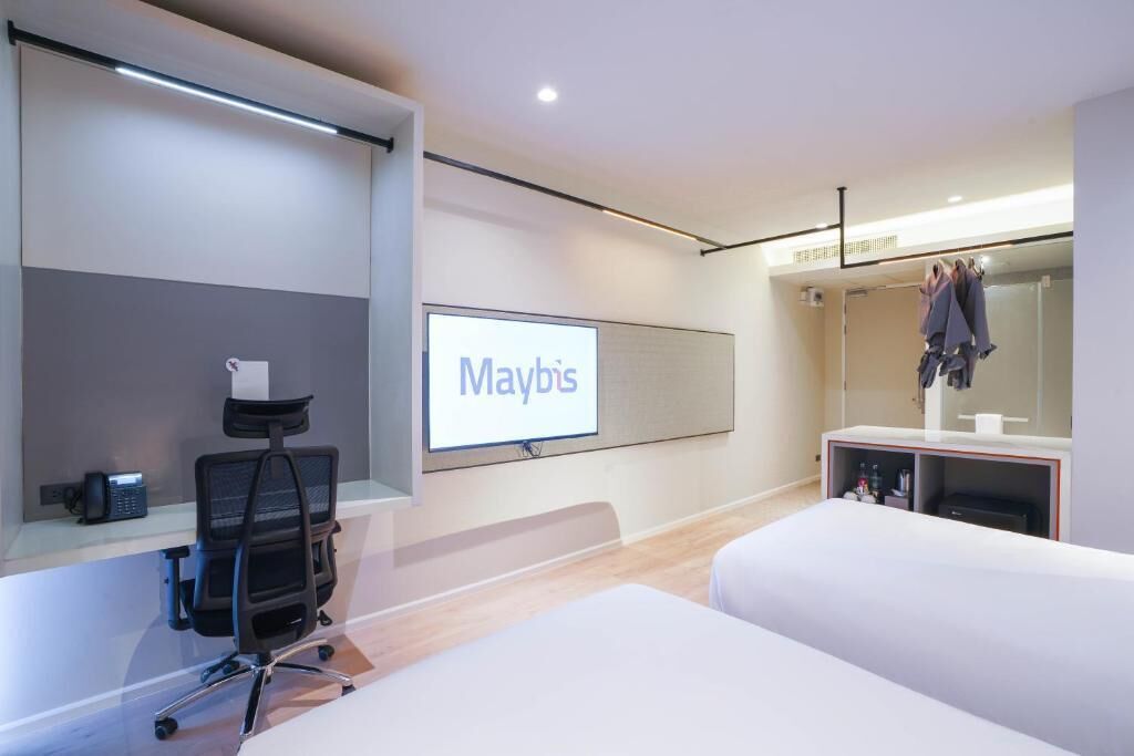 A modern hotel room with a bed, a desk with a chair, a flat-screen TV, and a wardrobe.