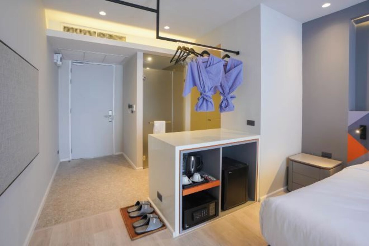 A hotel room with a bed, a small desk, a wardrobe, a shoe rack, and a shower area.