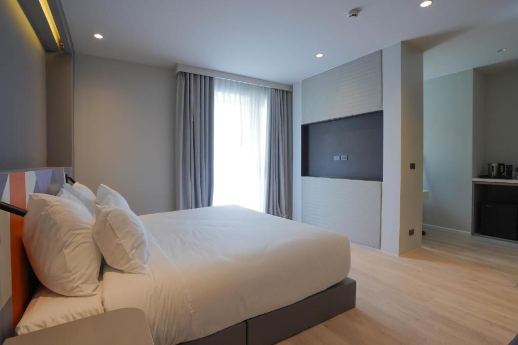 A modern hotel room with a large bed, a flat-screen TV mounted on the wall, and a small kitchenette area.