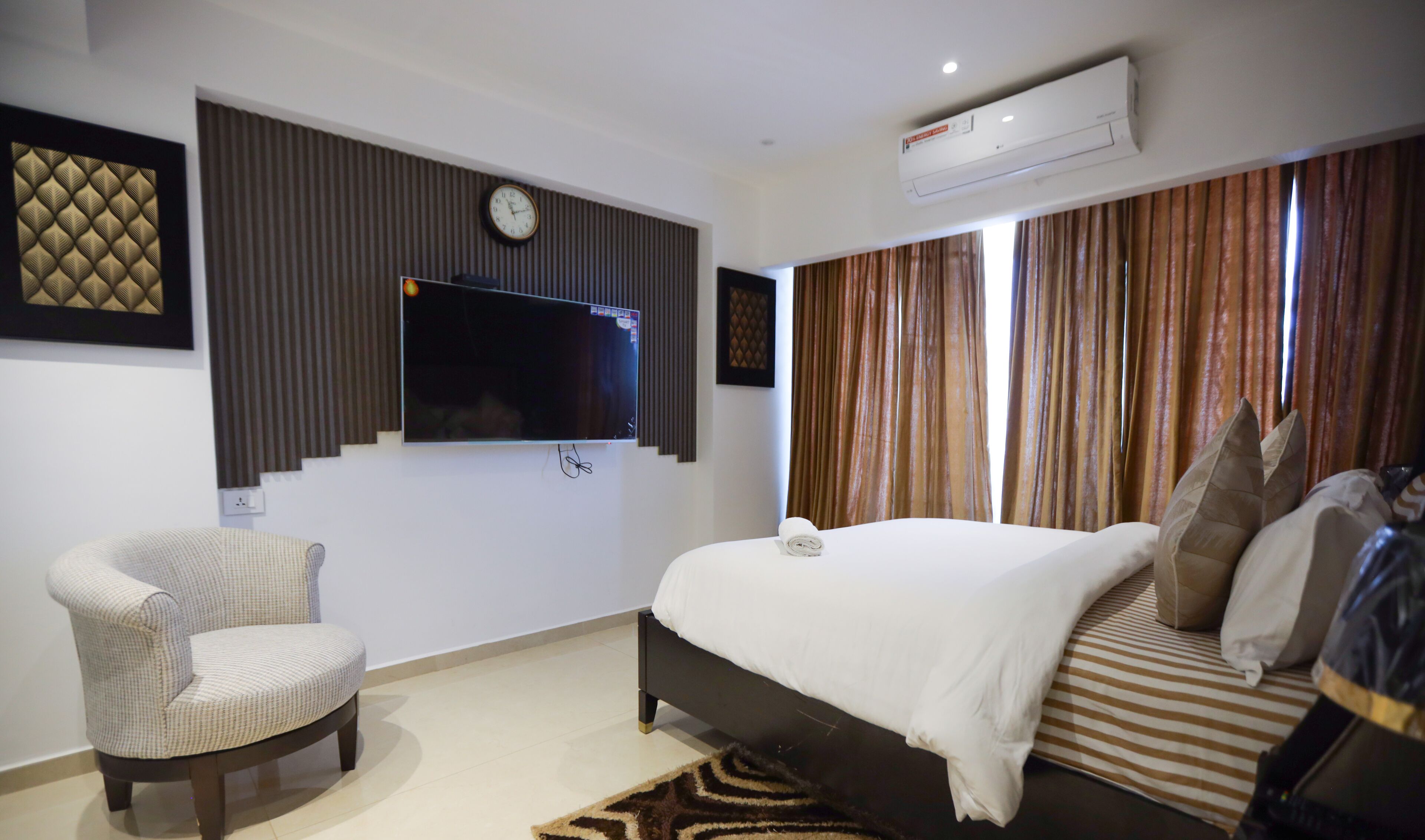 Une chambre d’hôtel équipée d’un lit, d’une chaise, d’un téléviseur à écran plat, d’une horloge et d’un appareil de climatisation.