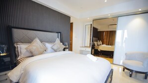 A modern hotel room with a large bed, a separate sitting area with a chair, and a view into another room. - Solaris Cozy Haven (Accra)