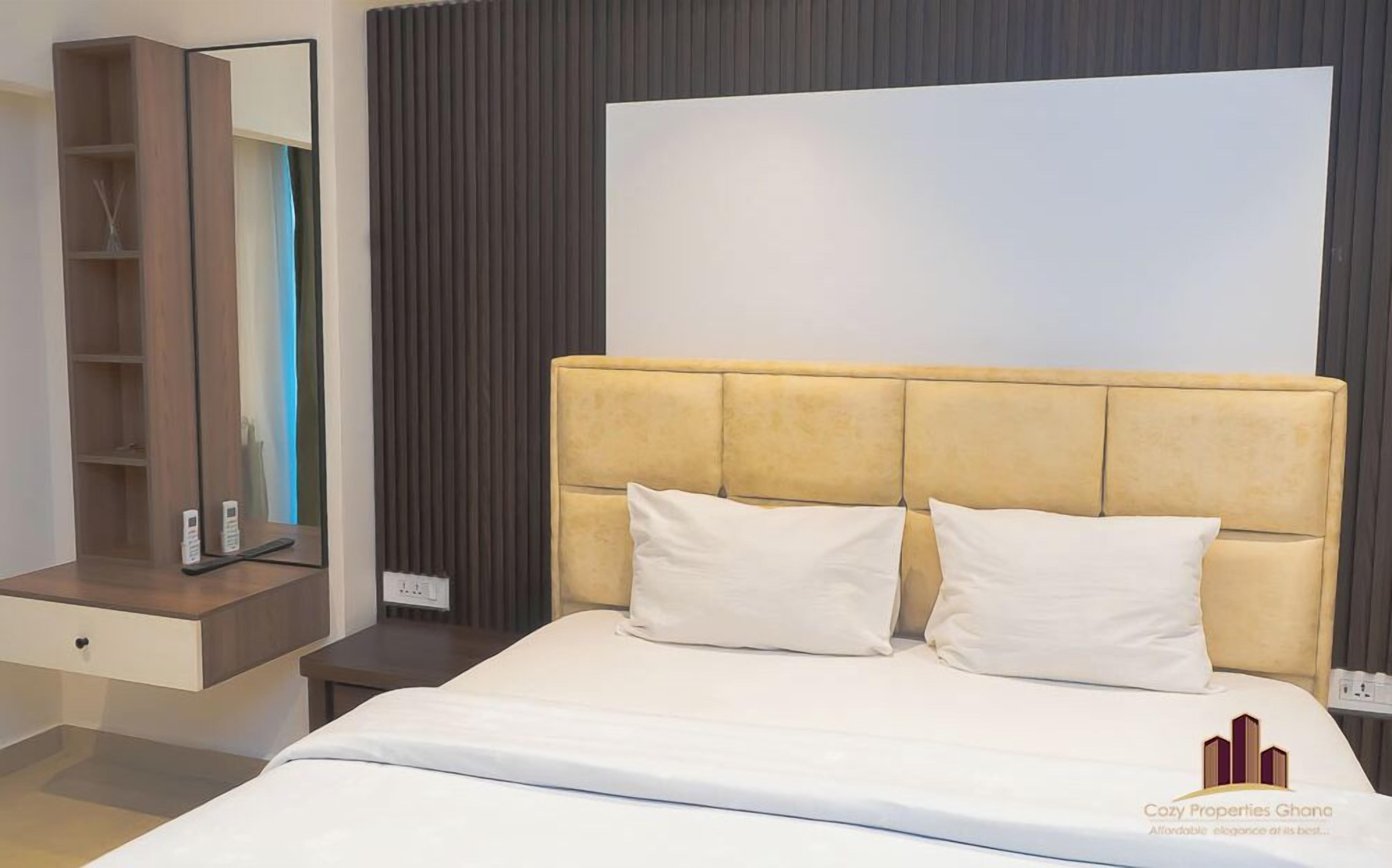 A hotel room with a bed, a nightstand, a mirror, and a wardrobe.