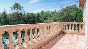A balcony with a stone balustrade overlooking a pool and lush greenery.