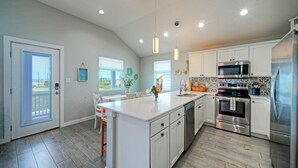 A modern kitchen with white cabinets, stainless steel appliances, and a large island. - Salty Texan by AvantStay | Central Location, Views (Port Aransas)