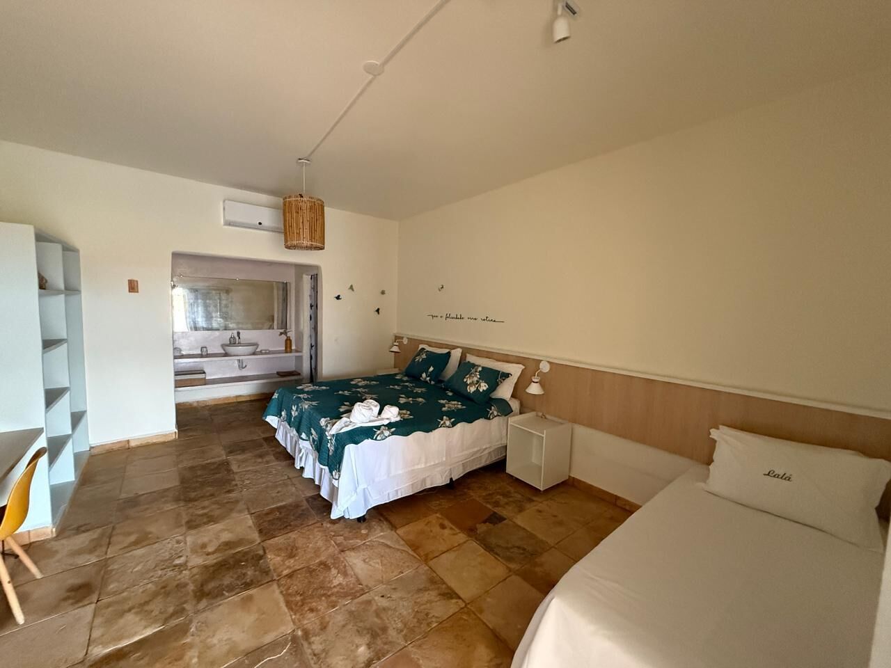 A bedroom with a bed, a bedside table, a chair, and a bathroom visible through an open door.