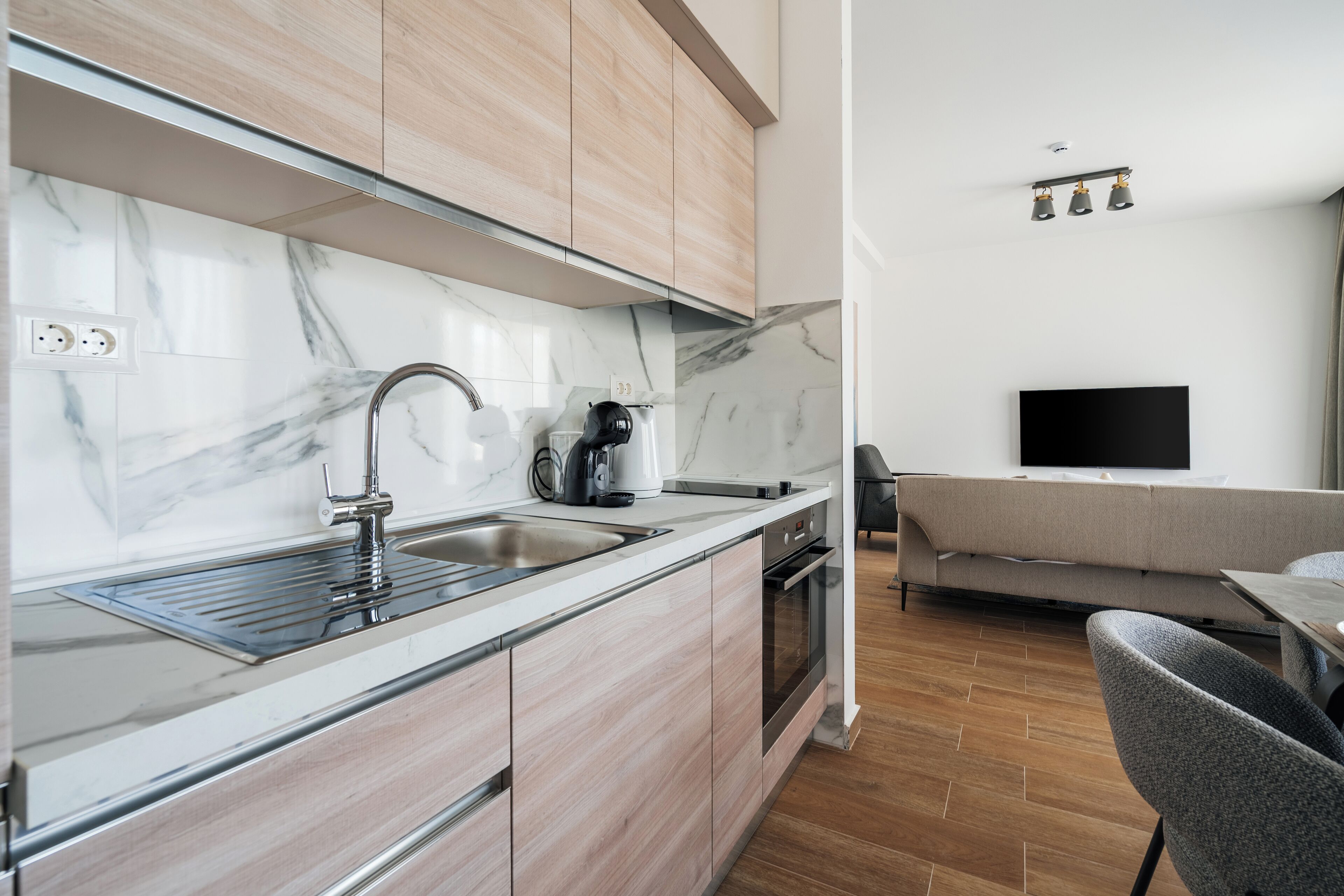 A modern kitchen with a marble backsplash, wooden cabinets, a stainless steel sink, and a built-in oven.