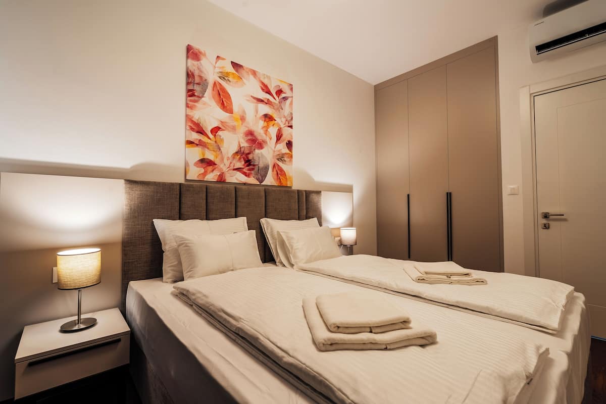 Une chambre d’hôtel avec deux lits, une grande œuvre d’art florale accrochée au mur, une table de chevet avec une lampe et une armoire.