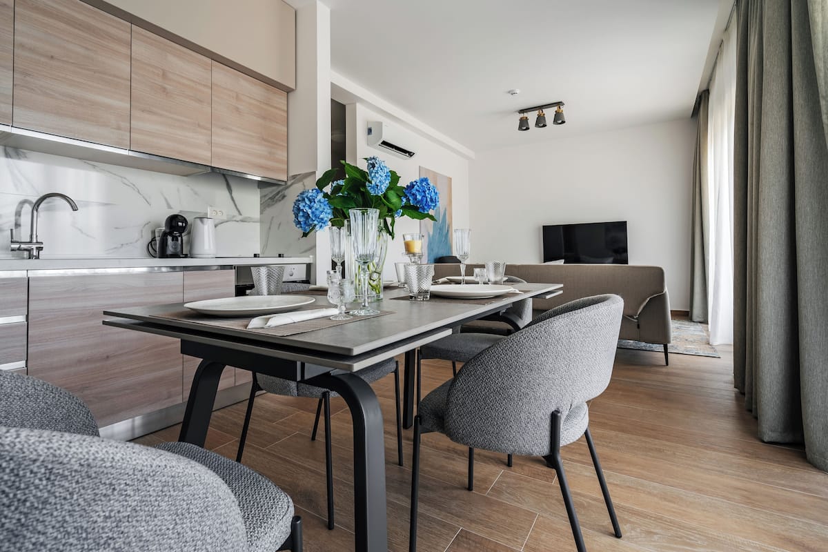 Une cuisine moderne avec un dosseret en marbre, un coin repas avec des chaises à revêtement gris et un salon avec un canapé et un téléviseur.