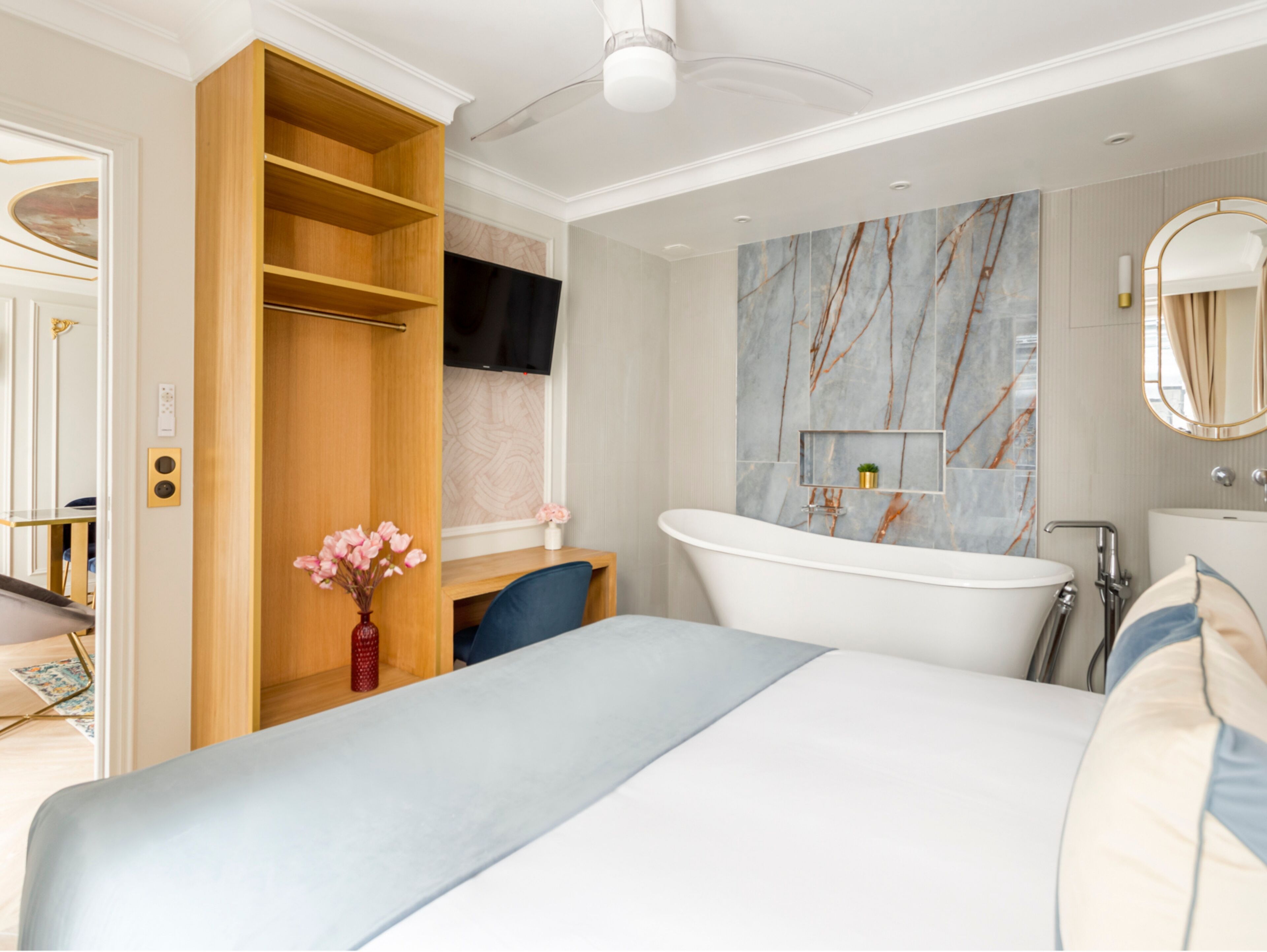 Une chambre moderne avec un grand lit, une armoire intégrée, une coiffeuse avec un pare-éclaboussures en marbre et une baignoire sur pieds.
