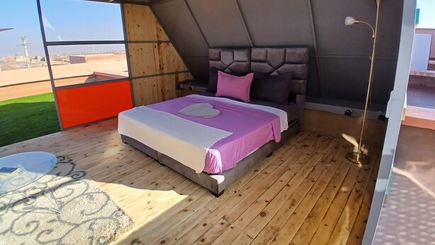 A tent-style room with a bed, a small table, and a view of the outside. - Chateau Nougat Marrakech (Tameslouht)