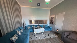A modern living room with a blue sectional sofa, a small dining table, and a patterned rug. - Chateau Nougat Marrakech (Tameslouht)