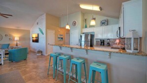 A modern kitchen with white cabinets, a stainless steel refrigerator, and a bar area with turquoise stools.