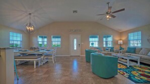 A spacious living room with a high ceiling, a dining area with a white table and benches, and a ceiling fan.