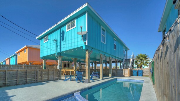 A turquoise house with a pool, wooden deck, and outdoor seating.