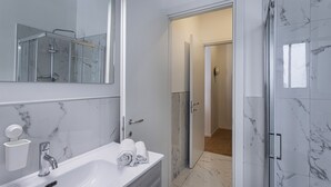 Un baño moderno con lavamanos blanco, un espejo grande y una zona de ducha.