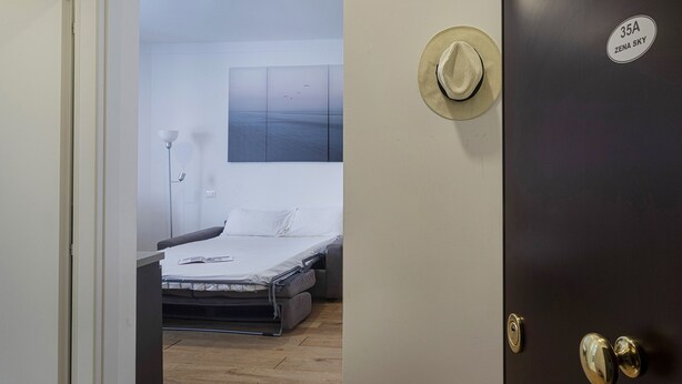 Una habitación con una cama, un sombrero colgado en la pared y una puerta con cerradura y una pegatina.