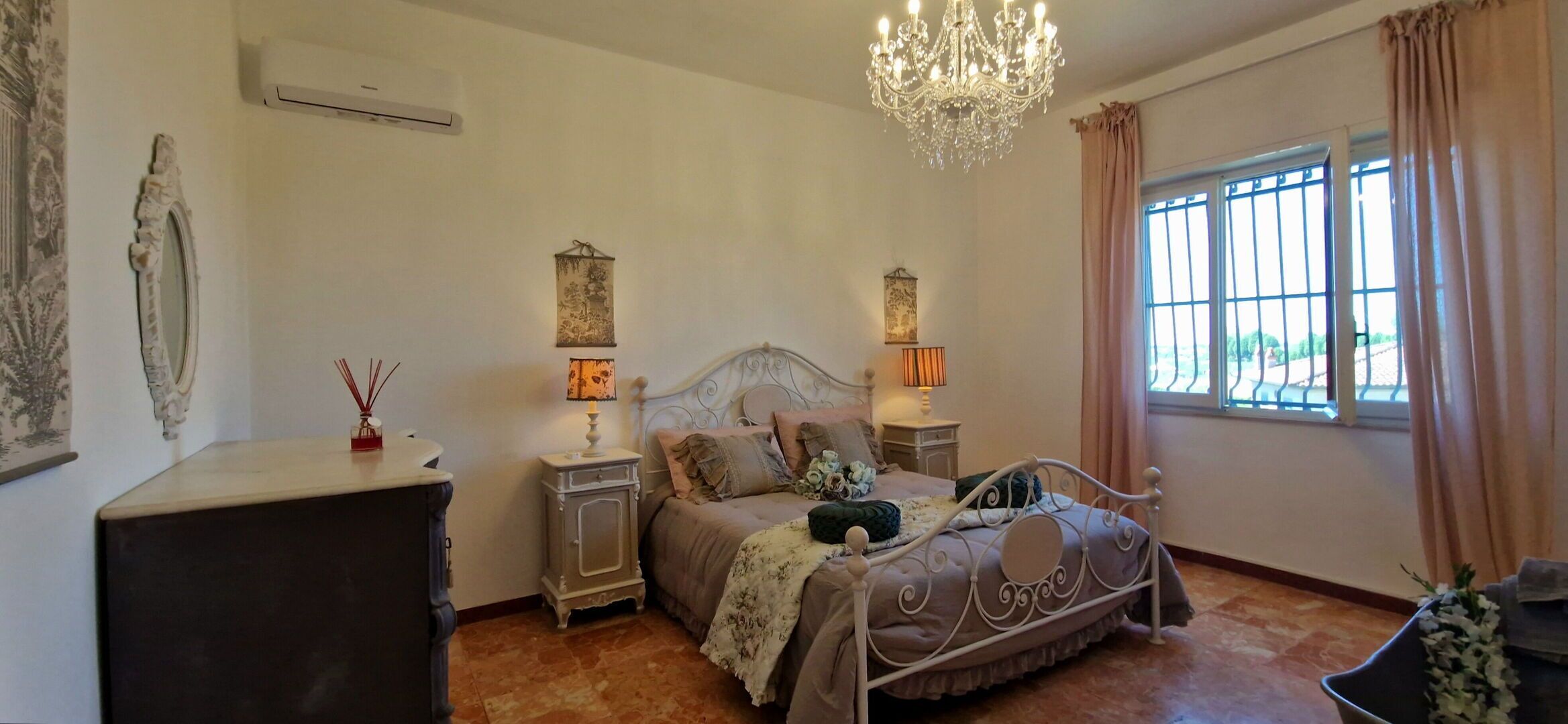 Une chambre à coucher comprenant un lit, deux tables de chevet, un lustre, une fenêtre avec des rideaux et un climatiseur fixé au mur.