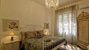 A bedroom with a bed, a chandelier, a wardrobe, and a nightstand with a lamp.