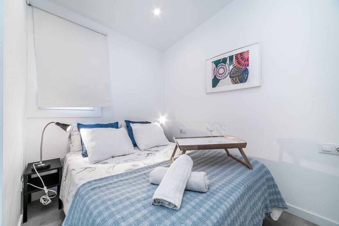 Una camera da letto con un letto, un comodino con una lampada, un tavolino con bicchieri e un quadro appeso al muro.