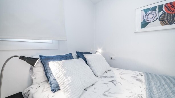 A bedroom with a bed, pillows, a bedside lamp, and a wall-mounted light fixture.