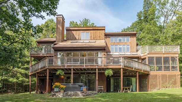 A two-story wooden house with a balcony, a hot tub, and a stone patio.