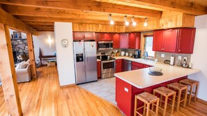 A modern kitchen with wooden beams, red cabinets, stainless steel appliances, and a central island with stools.