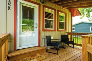 Eine Holzterrasse mit überdachter Veranda, einer weißen Tür mit rotem Zierstreifen und zwei schwarzen Stühlen.
